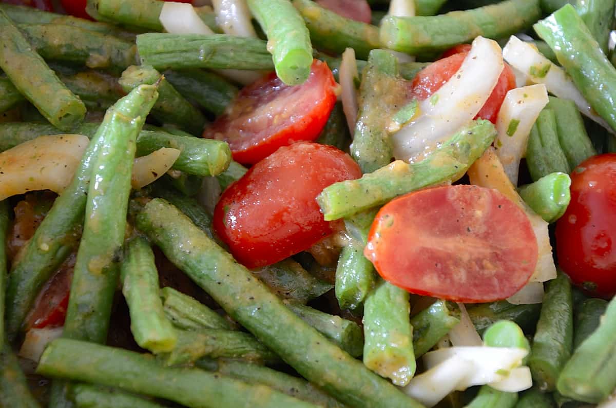 Close up of green string beans with sweet onions and cherry tomatoes in a Roasted Tomato Dressing.