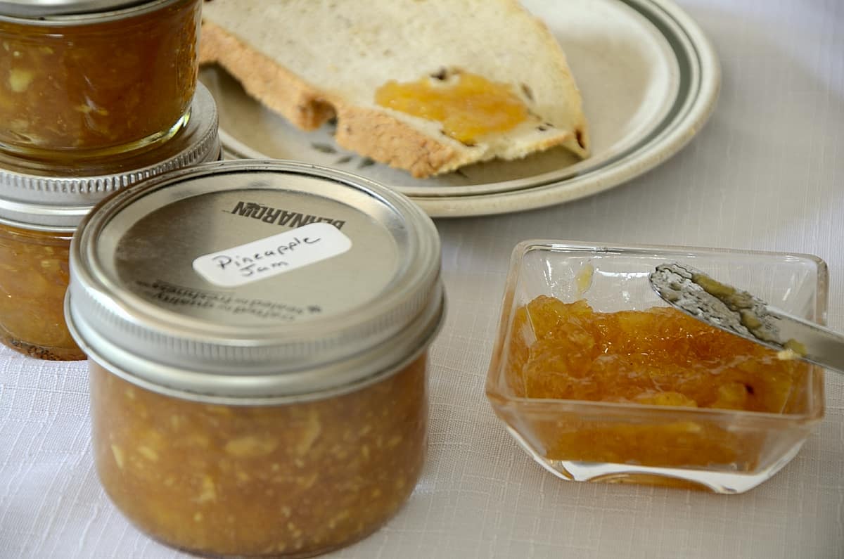 Small bowl of pineapple jam beside toast on a plate with a jar of jam on the side.