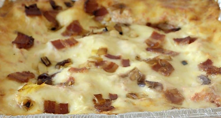 Close up of browned, melted cheesy, op layer of vegetable lasagna with bacon and onion bits.
