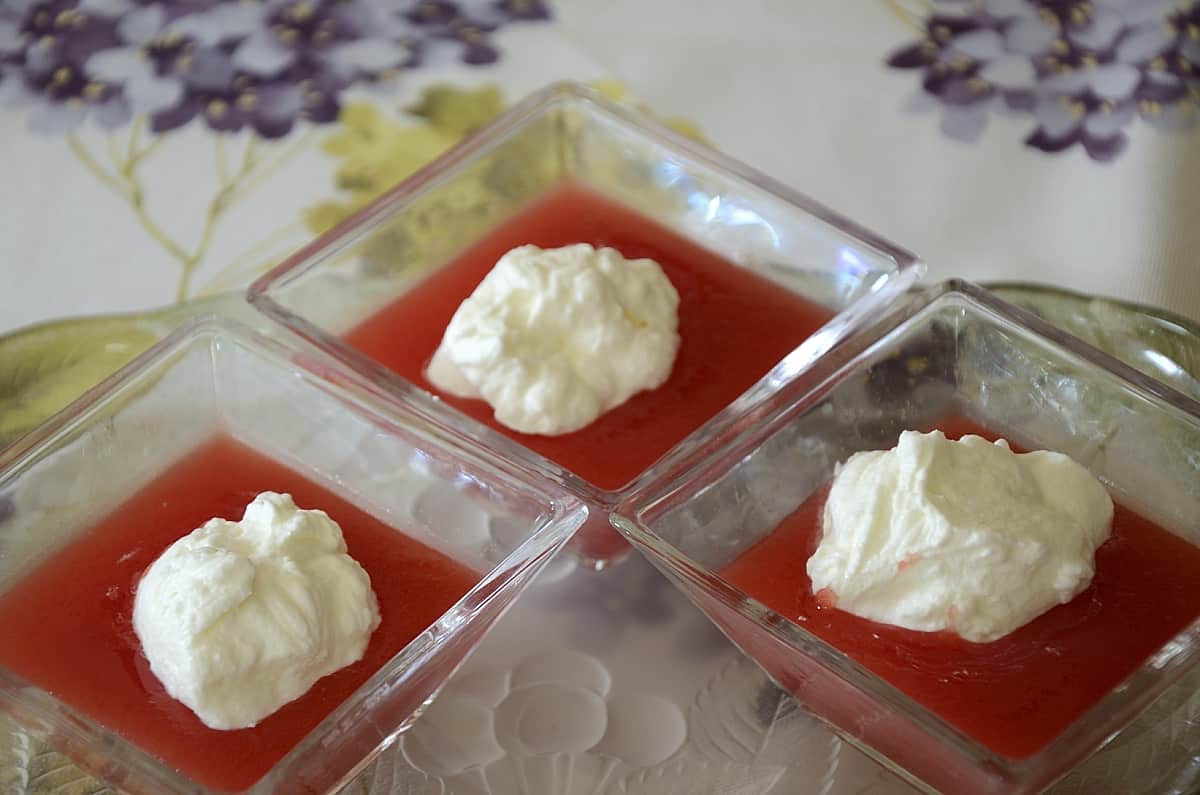 Small clear dishes with watermelon pudding topped with whipped cream.