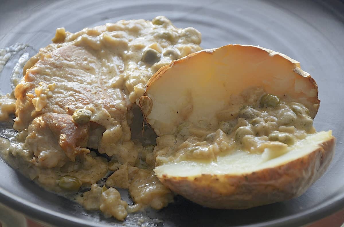 Golden seared pork chop with mustard caper pan sauce and a baked potato.