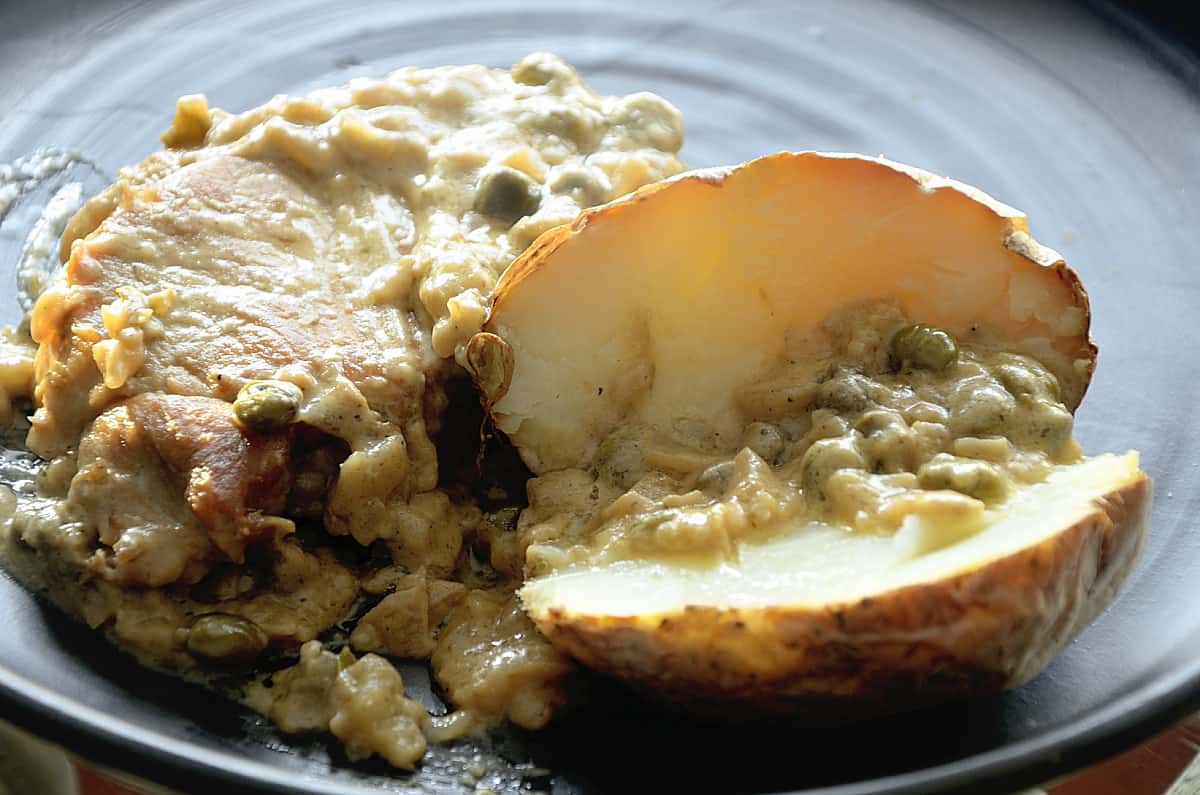 Golden seared pork chop with mustard caper pan sauce and a baked potato.