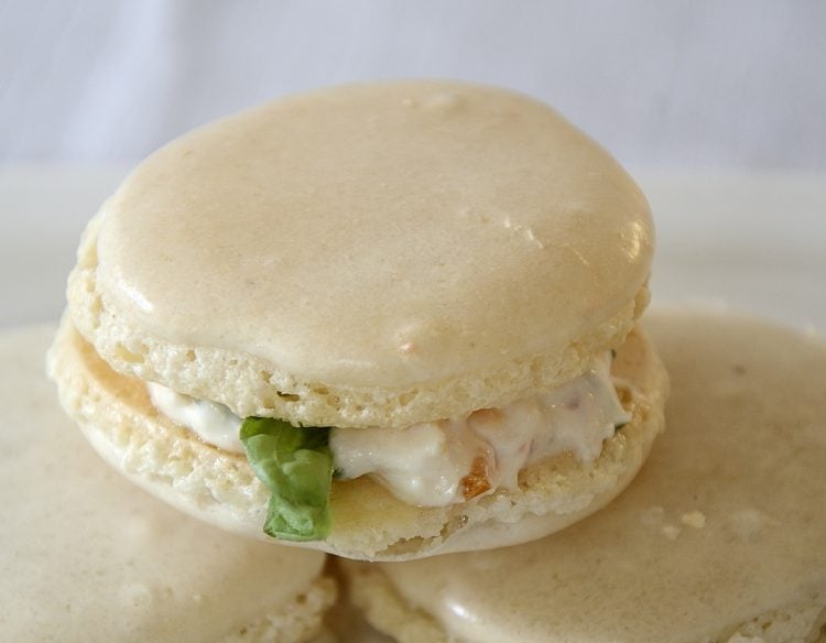 Almond Macarons filled with a feta, cream cheese mixture with tomato and basil, on a plate.
