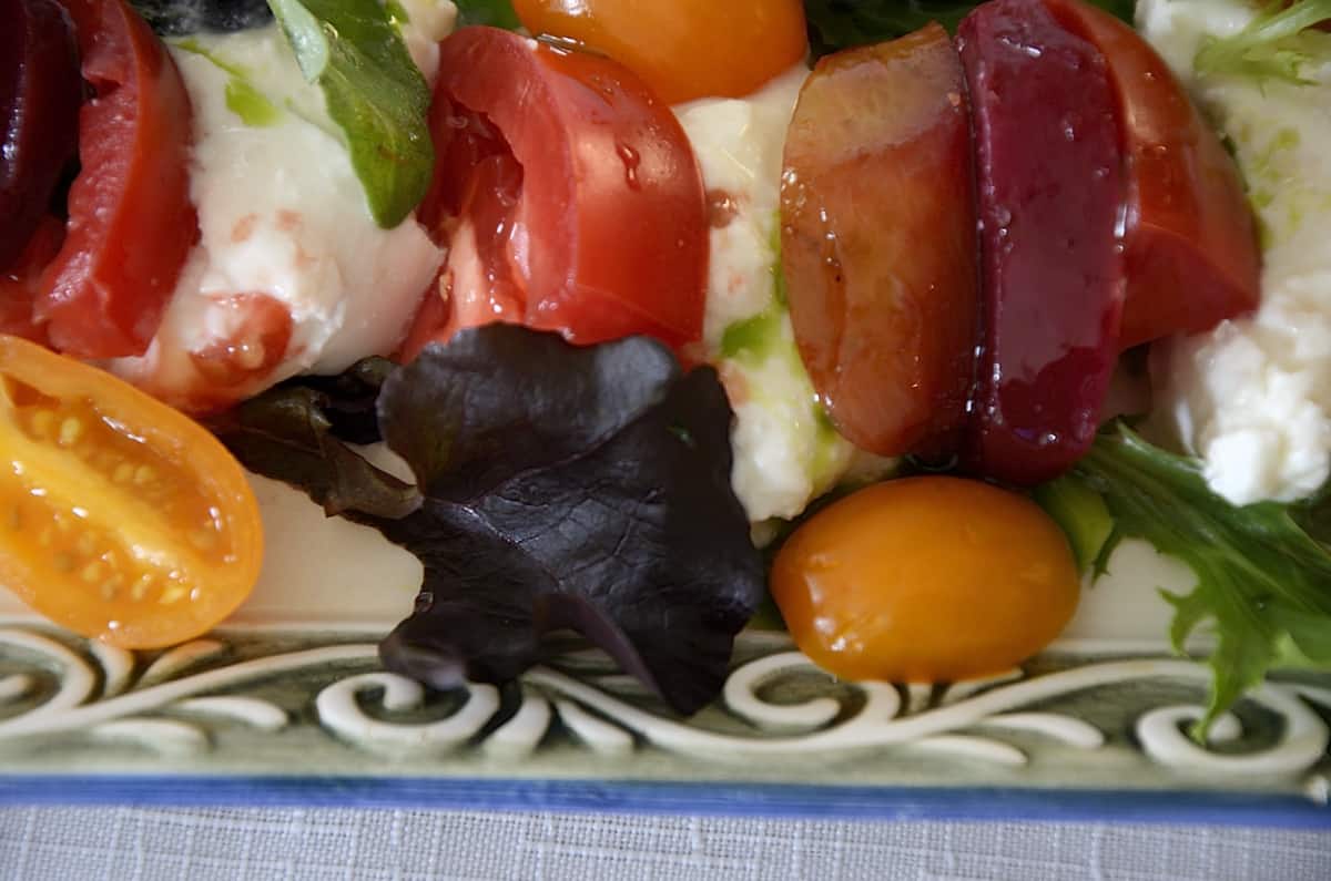 Side view of beet, heirloom  tomato and burrata wedges on a plate drizzled with vibrant green Basil Oil.