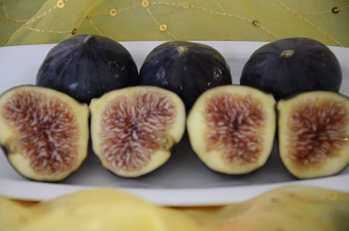 Fresh Black Mission Figs on a plate with some cut in half.