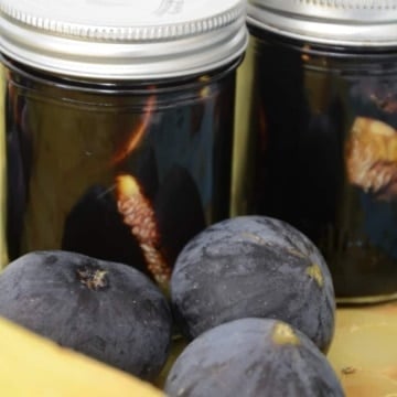 2 half pint jars of figs in balsamic vinegar mixture with fresh figs beside the jars.