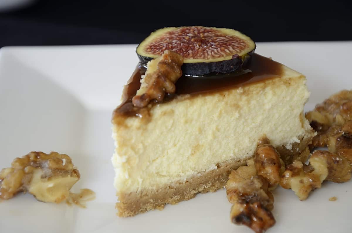 Piece of cheesecake drizzled with balsamic caramel and topped with fresh fig slices and candied walnuts.