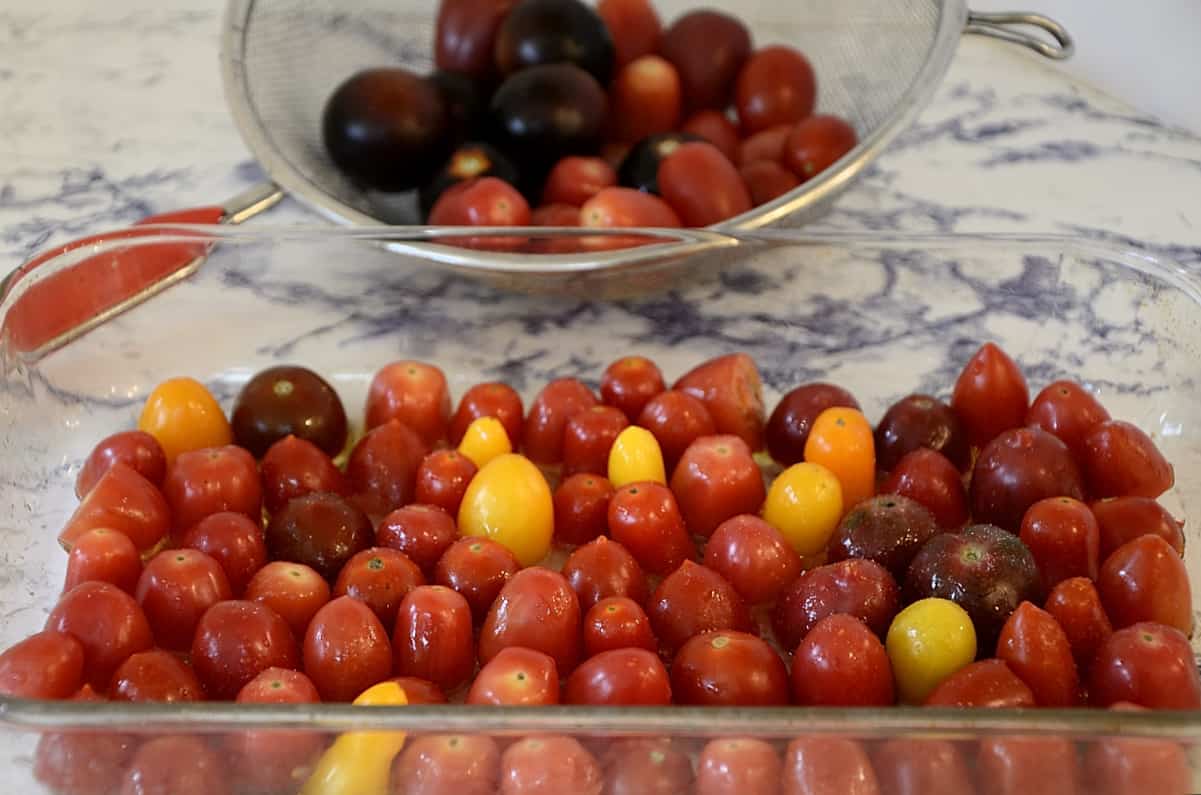 Cherry tomatoes halved in a baking dish, dirzzled with oil ready to roast in the oven.