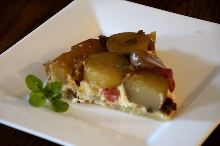 Slice of potato and cherry tomato tarte tatin on a plate with fresh oregano garnish.
