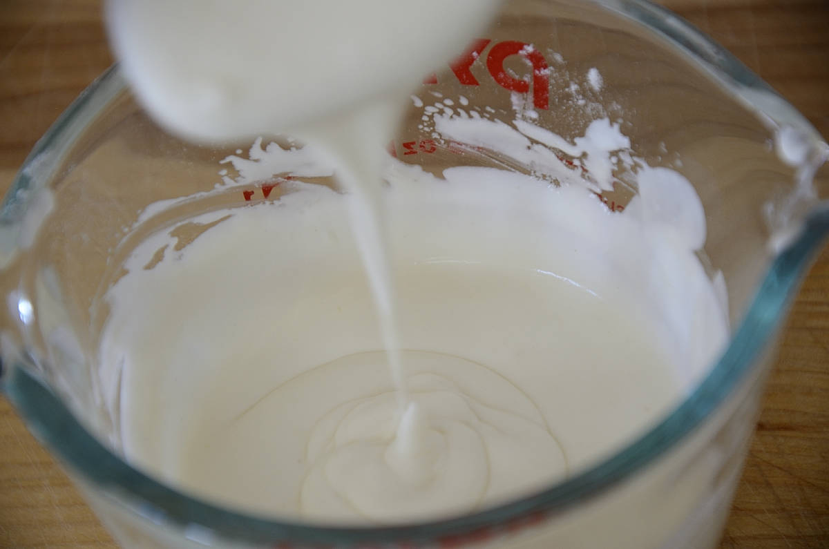 Sour cream dripping off a spoon into the container used to thicken it.