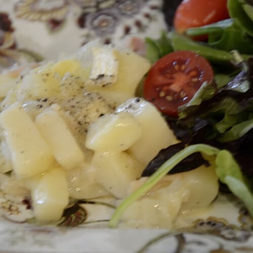 Creamy cubed potatoes in cheesy white wine sauce on a plate with a green side salad.