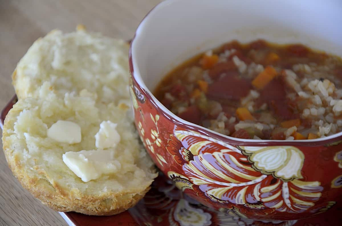 Buttermilk biscuit beside a bowl or tomato vegetable soup.
