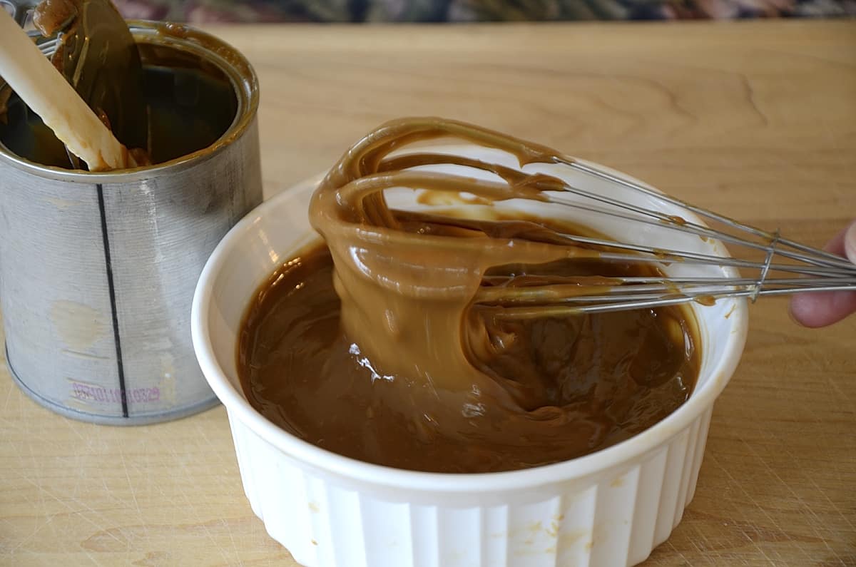 Caramel sauce dripping off a whisk over a ceramic bowl.