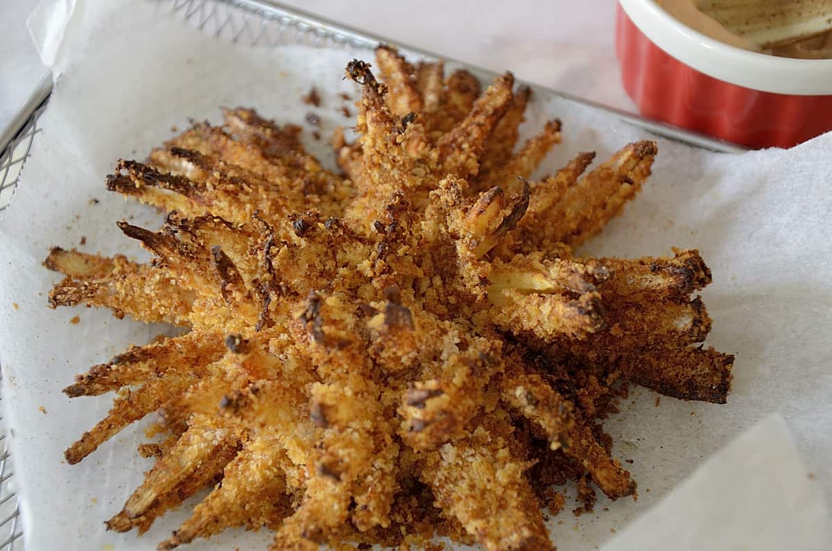 Crispy, breaded blooming onion with edge of the dipping sauce container beside.