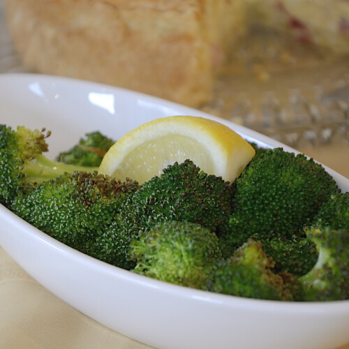 Air Fried broccoli florets in a serving bowl with lemon wedge.