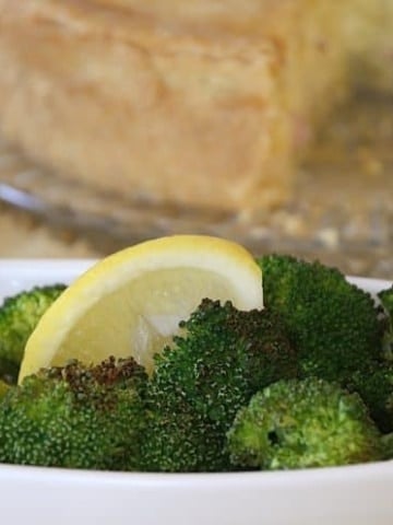 Air Fried broccoli florets in a serving bowl with lemon wedge.