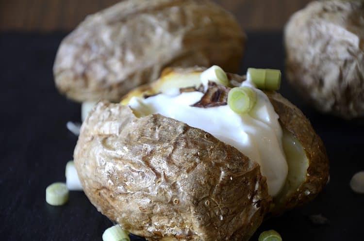 Crispy baked potato split open with sour cream and green onion toppings.