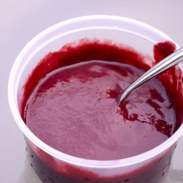 A container of smooth, thick and spicy blackberry sauce.