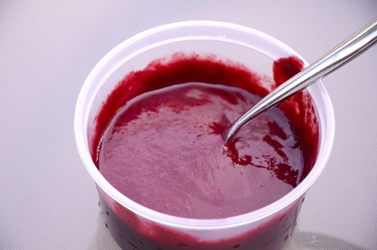 A container of smooth, thick and spicy blackberry sauce.