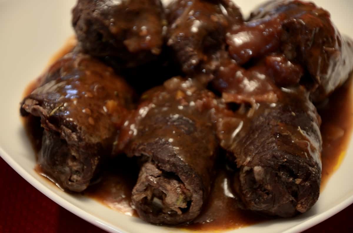 Deep brown rolled beef 'braciole' is rich tomato sauce in a serving dish.