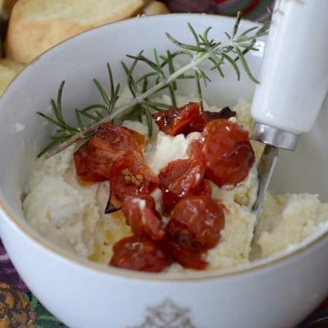 Close up of a small bowl of creamy feta dip topped with roasted grape tomatoes and sprig of rosemary.