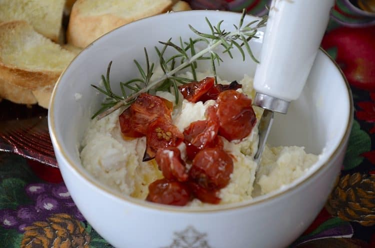 Close up of a small bowl of creamy feta dip topped with roasted grape tomatoes and sprig of rosemary.