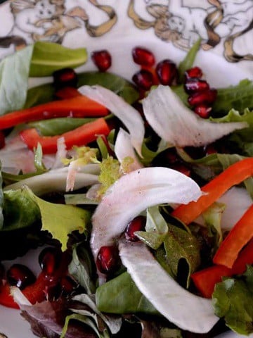 Fennel pomegranate salad on plate with red pepper slices and pomegranate arils.
