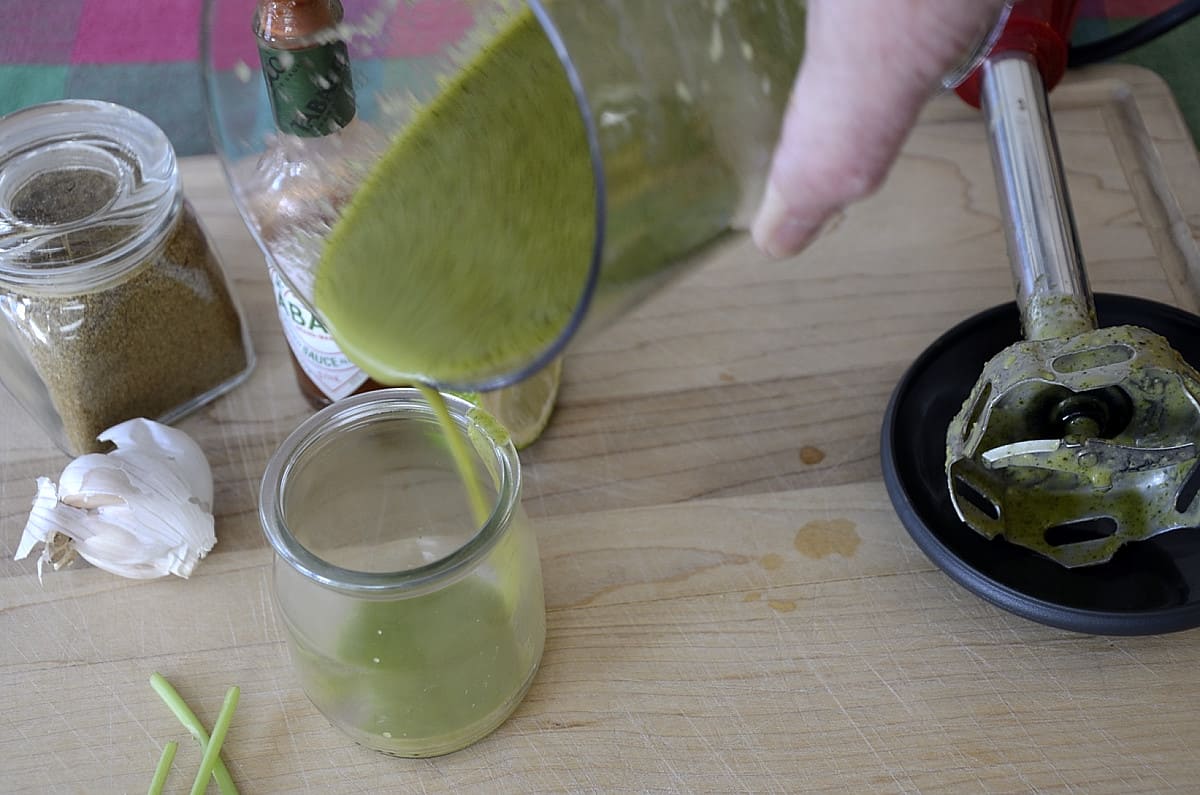 Bright green cilantro lime dressing being poured in to a small jug.