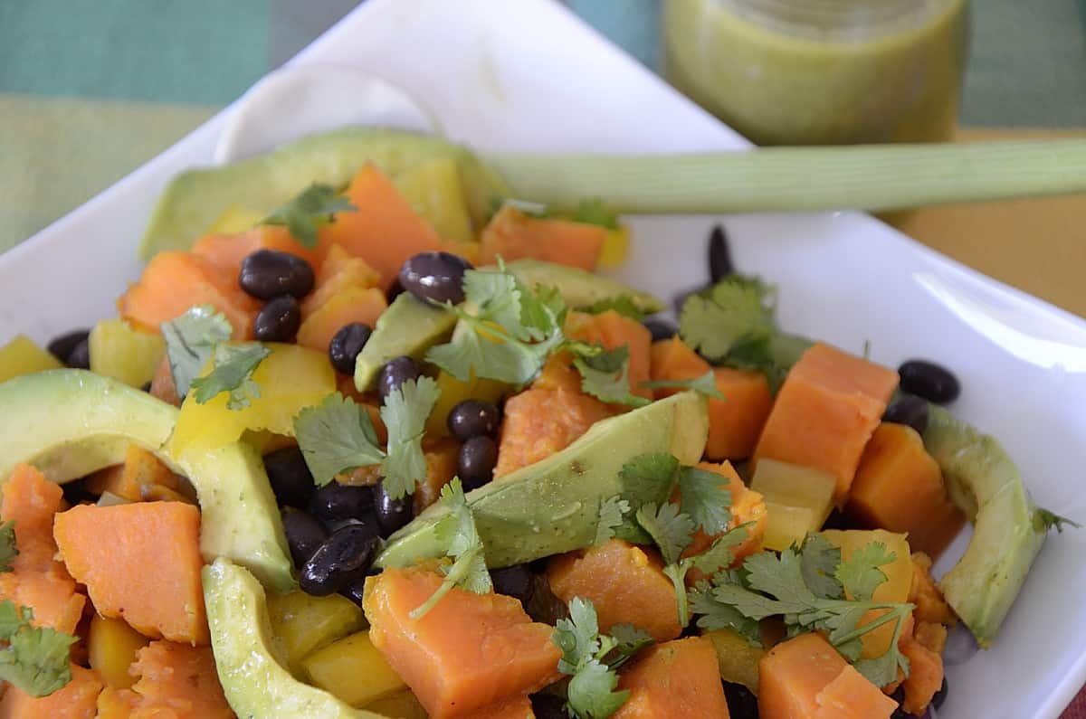 Bright orange sweet potato cubes, avocado and black beans mixed in a bowl with fresh cilantro garnish.