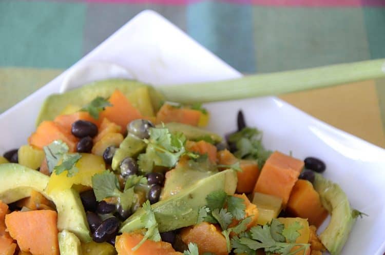 Bright orange sweet potato cubes, avocado and black beans mixed in a bowl with fresh cilantro garnish.