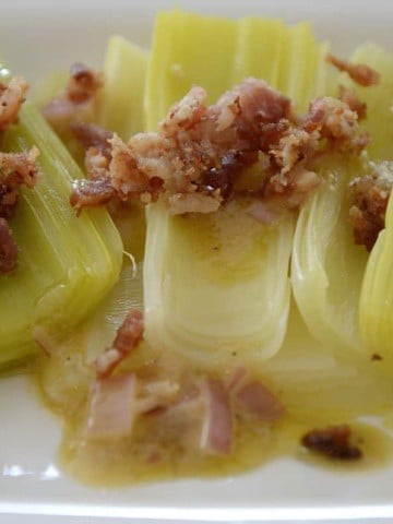 Steamed leeks fanned out on a serving platter topped with bacon bits and Shallot Mustard Vinaigrette.