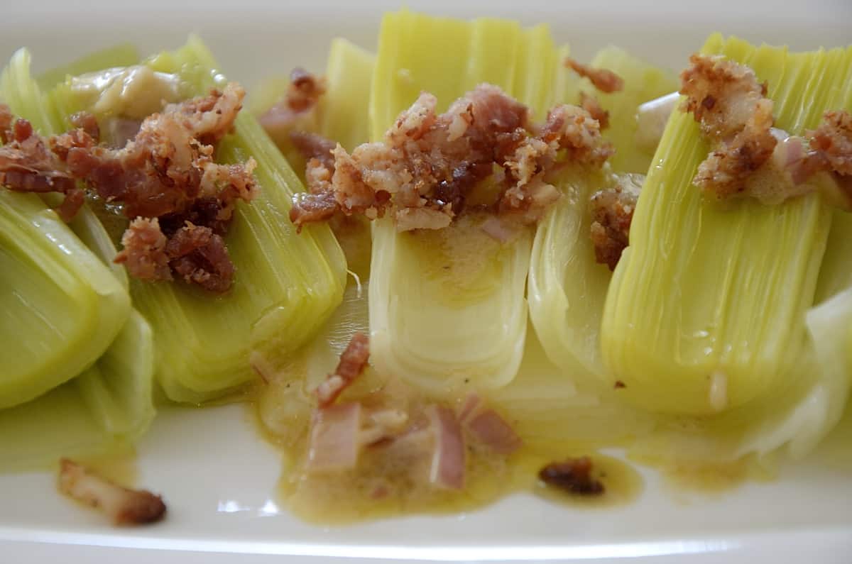 Steamed leeks fanned out on a serving platter topped with bacon bits and Shallot Mustard Vinaigrette.