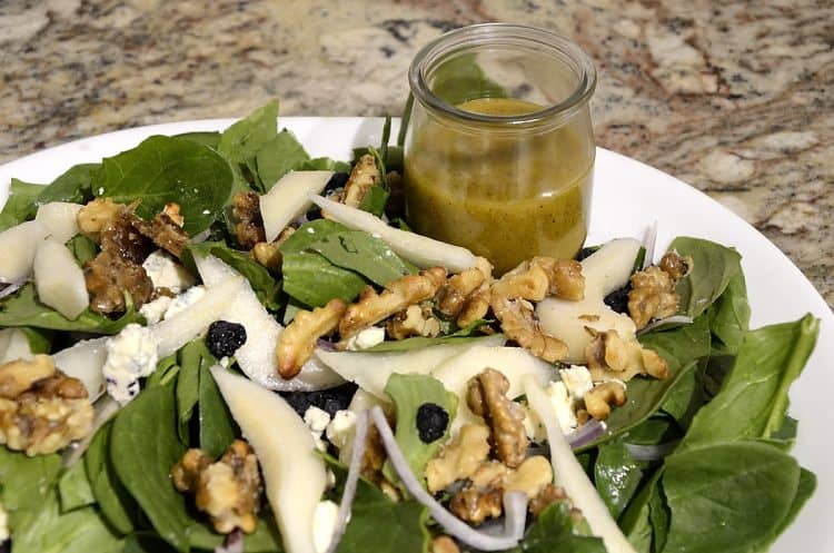 Close up of bed of spinach with pear, candied walnuts and dried blueberries toppings and honey mustard dressing.