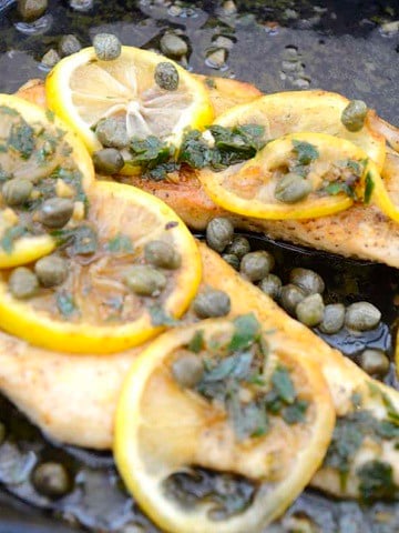 Browned chicken cutlet in buttery lemon sauce garnished with capers and parsley.