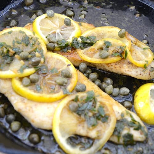 Browned chicken cutlet in buttery lemon sauce garnished with capers and parsley.