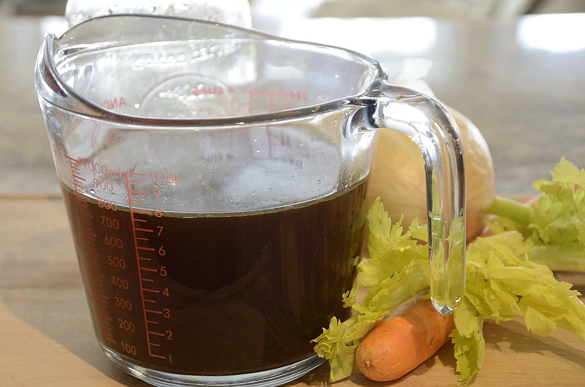 Dark brown roasted vegetable broth with a carrot and some celery beside it.