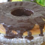 Cannoli bundt cake on a cake stand with shiny, chocolate ganache poured over it.
