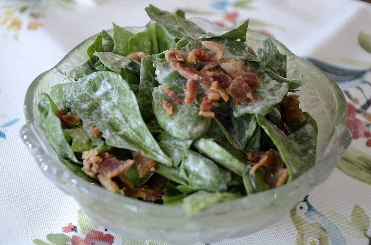 Close up of baby spinach and crispy bacon bits tossed in a creamy dressing.