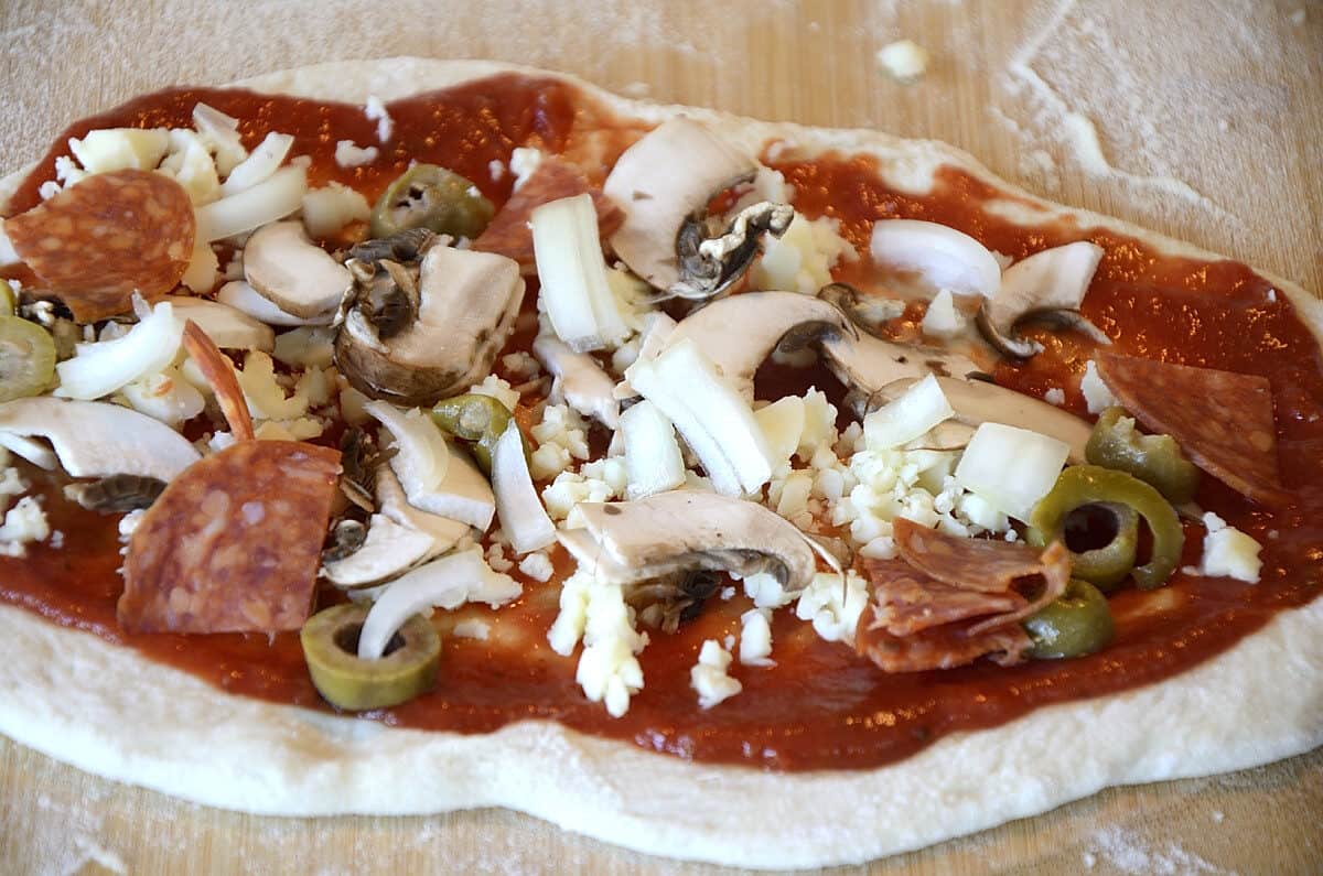 Uncooked pizza with tomato sause, mushrooms, pepperoni, olives and onions.