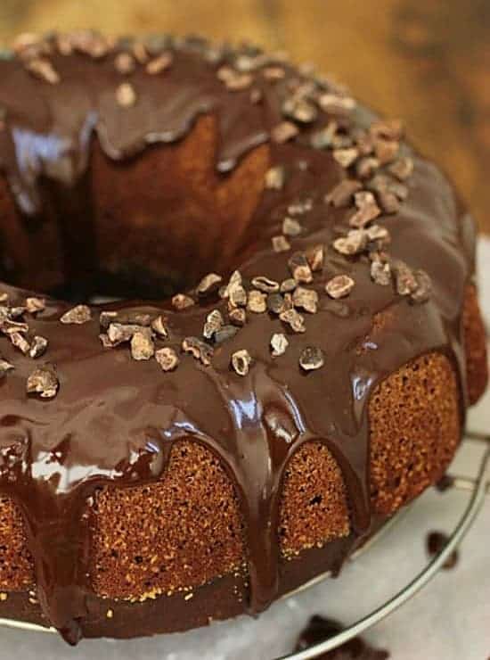 Chocolate Bundt cake drizzled with glossy chocolate icing on a cake plate.