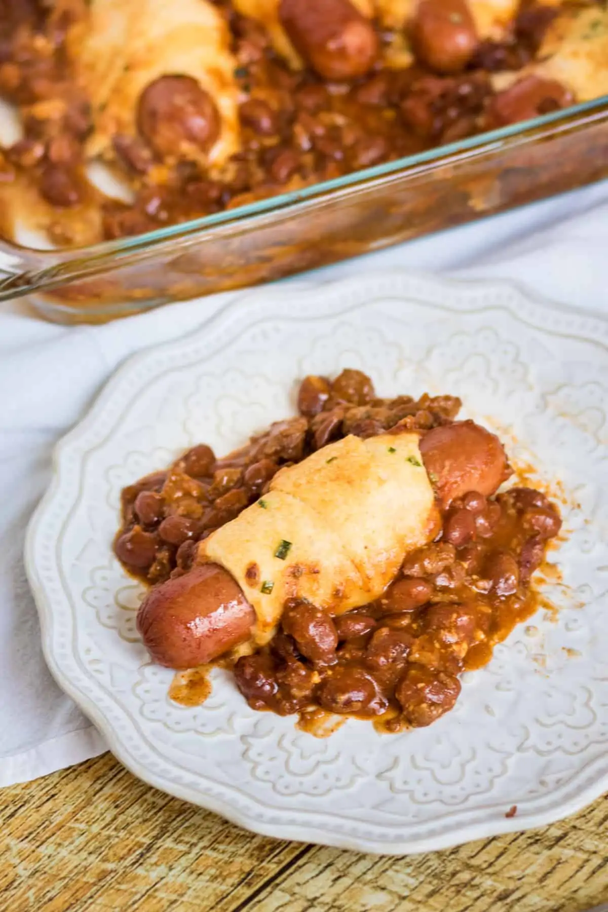 Plate with a chili cheese dog on top of a mound of chili.