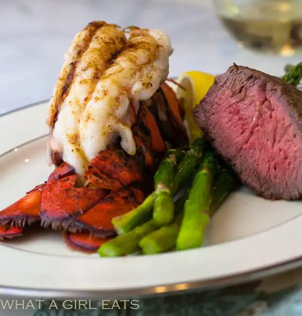 Broiled lobster tail on a plate with rare steak and asparagus.