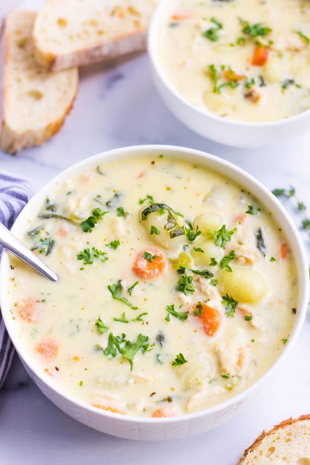 Bowl of creamy soup with gnocchi, chicken, carrots and parsley.