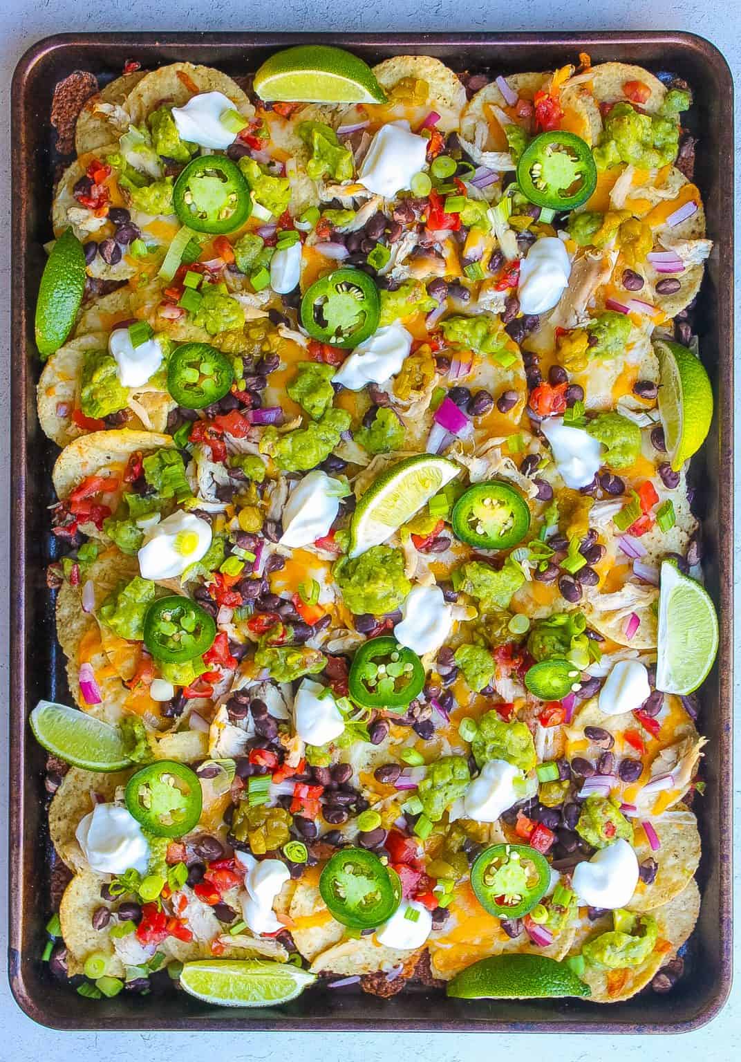 Sheet pan of nachos loaded with shredded chicken, jalapenos, black beans and lime.