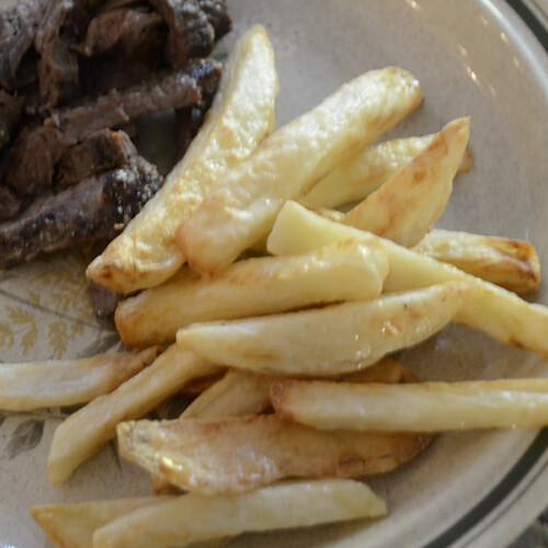 Golden crispy salt and vinegar fries on a plate beside a steak.