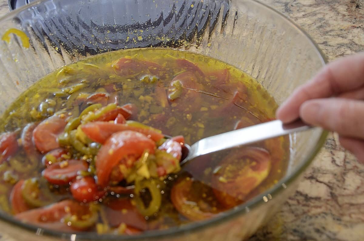 Bowl of quartered tomatoes with jalapenos, onions, oil and spices.