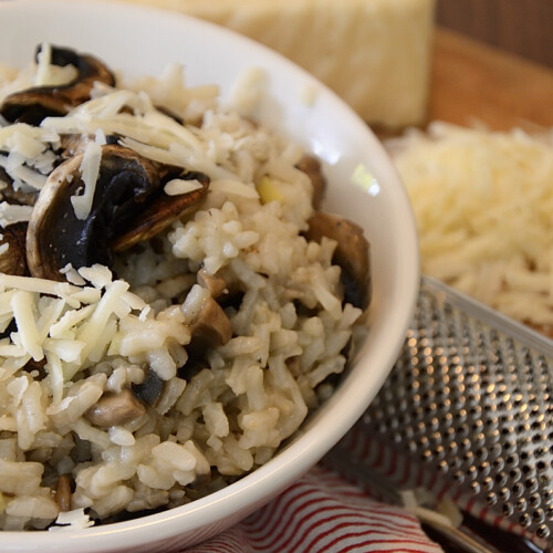 A bowl of risotto with roasted mushrooms on top and garnished with fresh grated Asiago cheese.