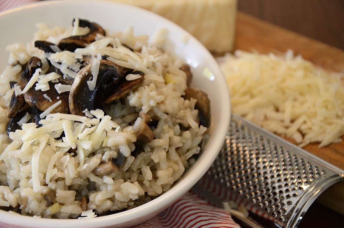 A bowl of risotto with roasted mushrooms on top and garnished with fresh grated Asiago cheese.