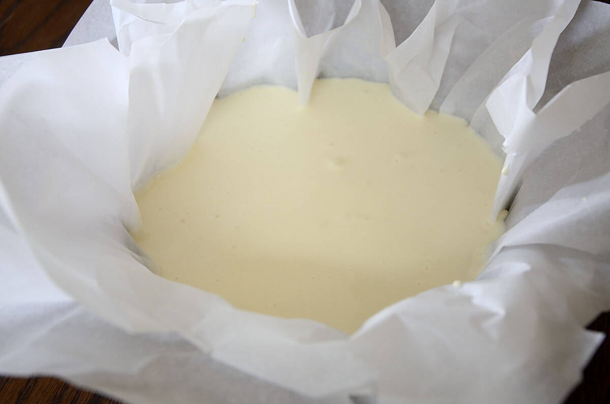 Parchment lined springform pan full or cheesecake mixture for burnt basque cheesecake.