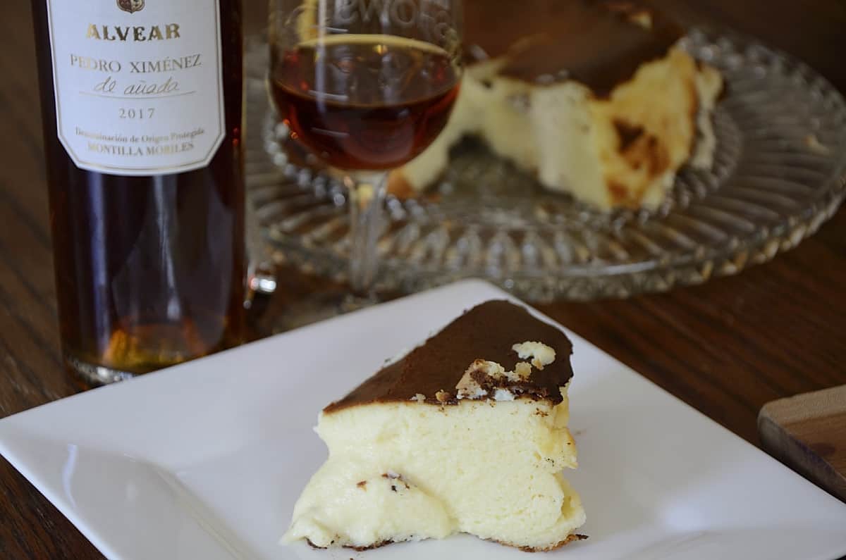 Piece of burnt Basque Cheesecake on a plate with Pedro Ximenez sherry beside.